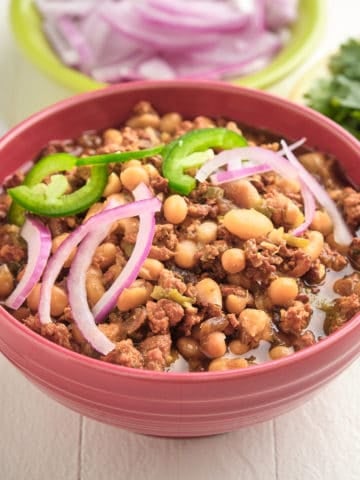 A bowl of white chili with sliced onions and jalapeños on top