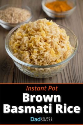 A bowl of brown basmati rice with uncooked rice and ground turmeric in the background