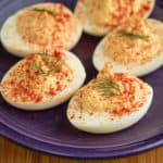 A plate of horseradish deviled eggs sprinkled with paprika and topped with a sprig of dill