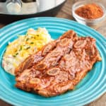 A plate with BBQ short ribs and mashed potatoes, with a dish of BBQ rub and a pressure cooker in the background