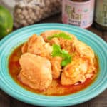 A plate of coconut curry chicken thighs with Thai curry paste and a lime in the background