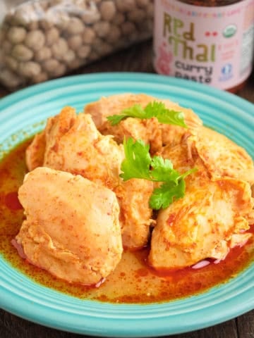 A plate of coconut curry chicken thighs with Thai curry paste and a lime in the background