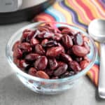 A bowl of cooked Ayocote Negro beans, with a spoon, a napkin, and a pressure cooker in the background