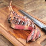 A tomahawk steak on a cutting board, with slices showing medium-rare doneness, and a slicing knife in the background