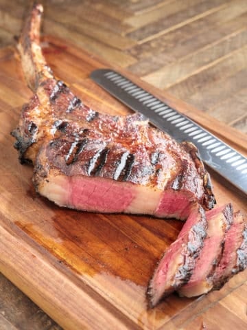 A tomahawk steak on a cutting board, with slices showing medium-rare doneness, and a slicing knife in the background