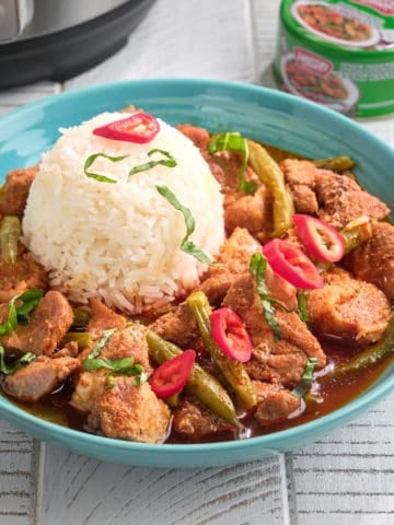 A bowl of prik king pork curry with a scoop of rice, topped with slivered basil and Thai red peppers