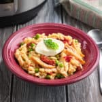 A bowl of rotisserie chicken risotto,topped with shredded chicken,peas,fresh mozarella,and a bay leaf.