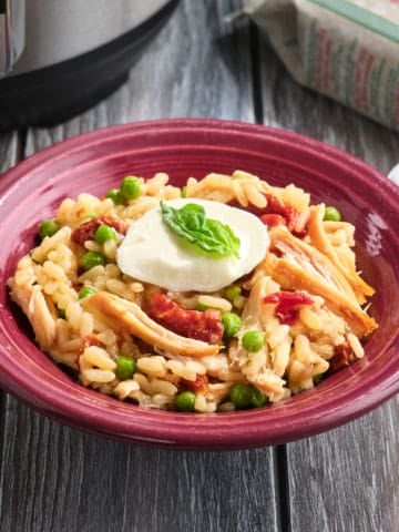 A bowl of rotisserie chicken risotto, topped with shredded chicken, peas, fresh mozarella, and a bay leaf.