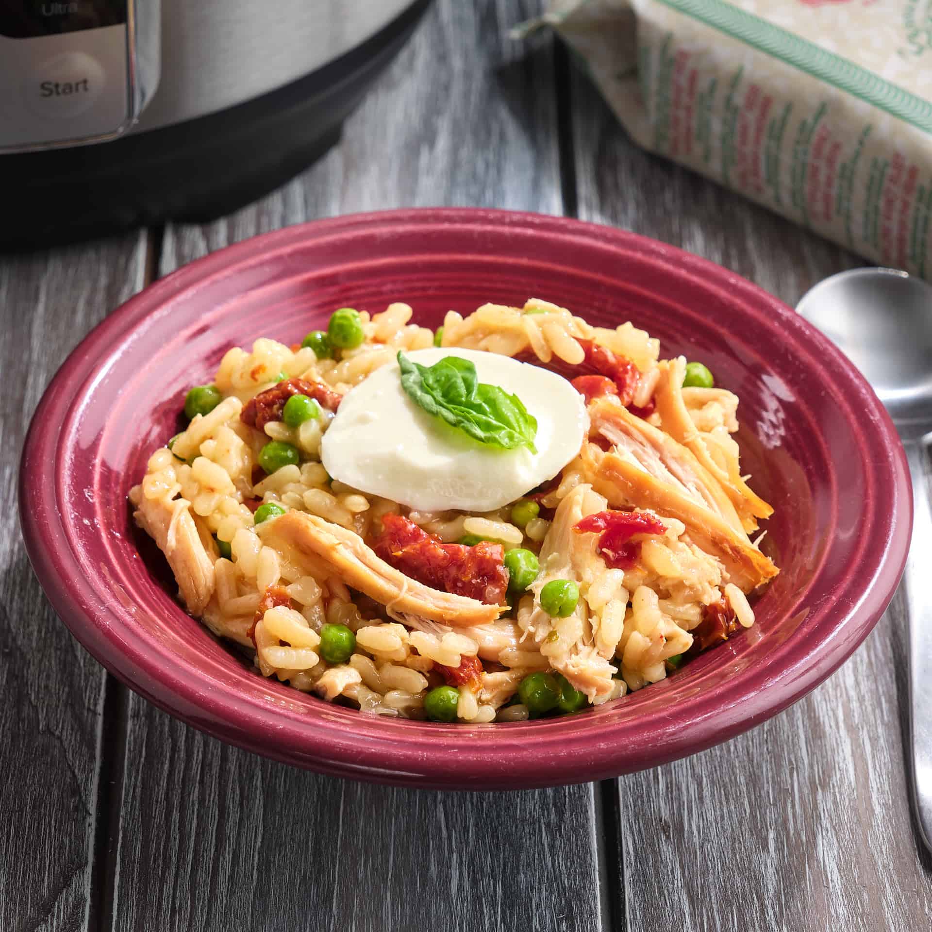 A bowl of rotisserie chicken risotto, topped with shredded chicken, peas, fresh mozarella, and a bay leaf.