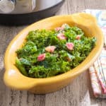 A bowl of cooked kale and pancetta, with a napkin and an Instant Pot in the background