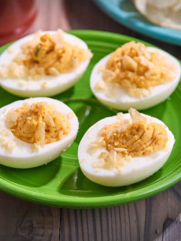 A plate of deviled eggs topped with crushed potato chips, with more potato chips and some paprika in the background