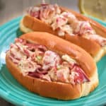 Two lobster rolls on an aqua plate, with a lemon in the background