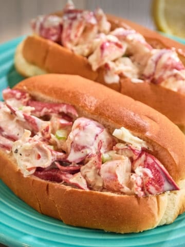 Two lobster rolls on an aqua plate, with a lemon in the background