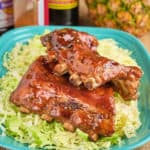 A plate of Hawaiian BBQ ribs, with a pineapple, sauces, and rub in the background