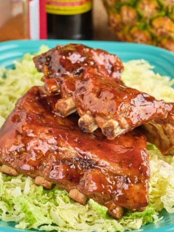 A plate of Hawaiian BBQ ribs, with a pineapple, sauces, and rub in the background