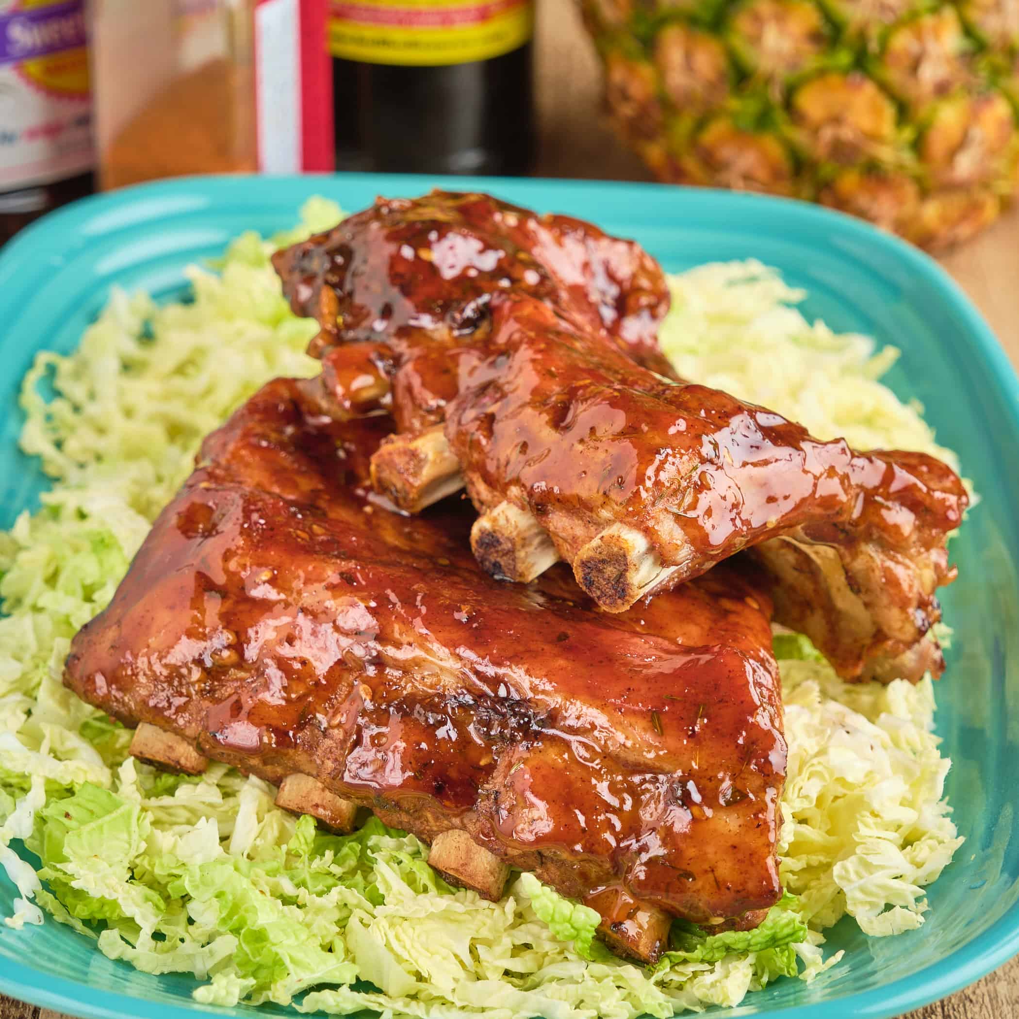 A plate of Hawaiian BBQ ribs, with a pineapple, sauces, and rub in the background