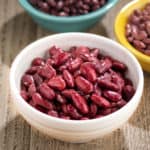 A bowl of cooked red kidney beans, with uncooked red kidney beans in the background