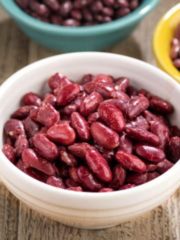 A bowl of cooked red kidney beans, with uncooked red kidney beans in the background