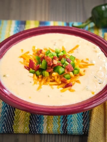 A bowl of chicken jalapeño popper soup, with a jalapeno, spoon, and napkin in the background