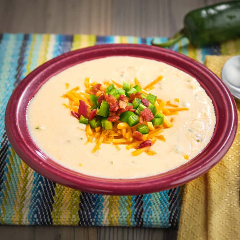 A bowl of chicken jalapeño popper soup, with a jalapeno, spoon, and napkin in the background