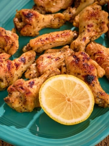 A platter of lemon pepper chicken wings, with a lemon half