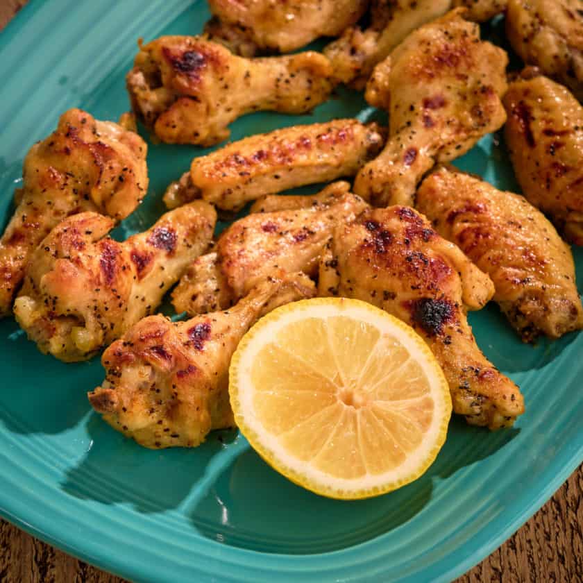 A platter of lemon pepper chicken wings, with a lemon half