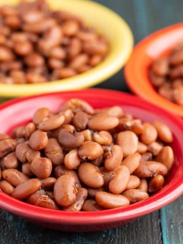 Three bowls of cooked Pinto Beans on a wood table