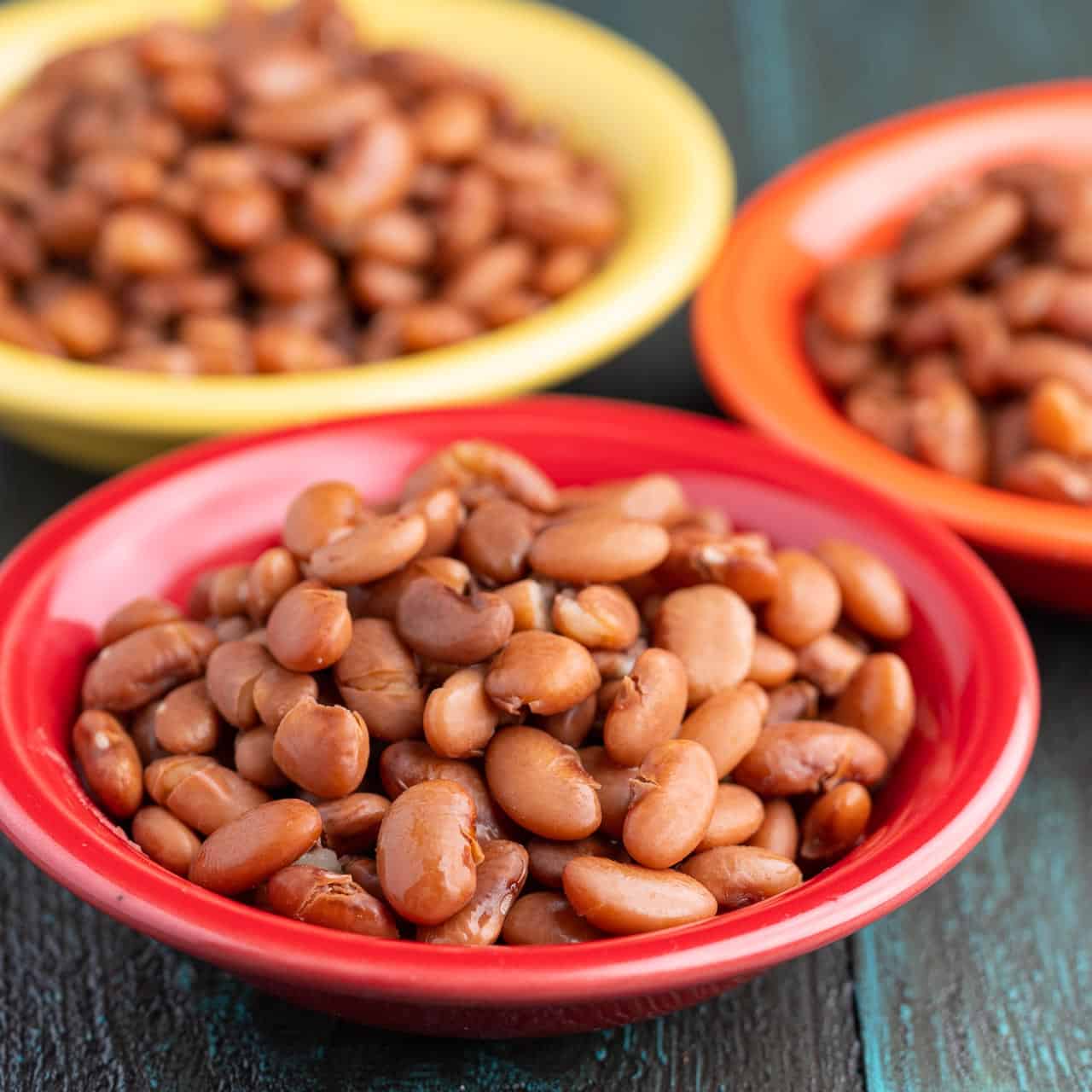 Three bowls of cooked Pinto Beans on a wood table