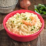 A bowl of shrimp risotto, with parsley, shallot, and uncooked rice in the background.