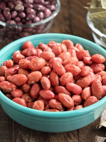 A bowl of cooked whipple beans, with uncooked beans and bay leaves in the background