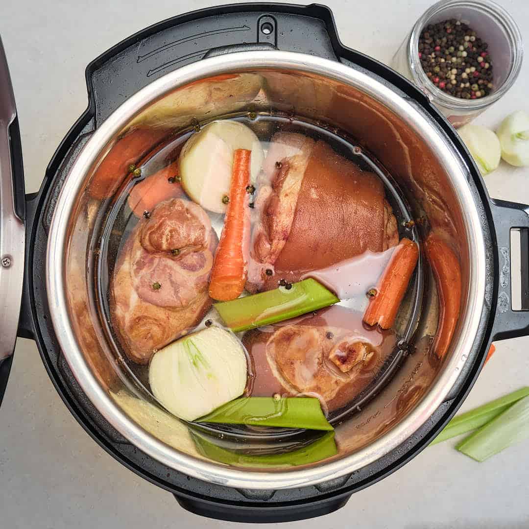 An Instant Pot full of ham hocks, vegetables, peppercorns, and water, ready to make broth