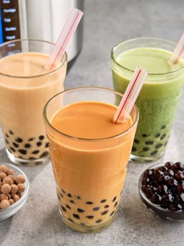 Three colorful glasses of boba tea, with cooked and uncooked boba pearls in dishes, and an Instant Pot in the background.