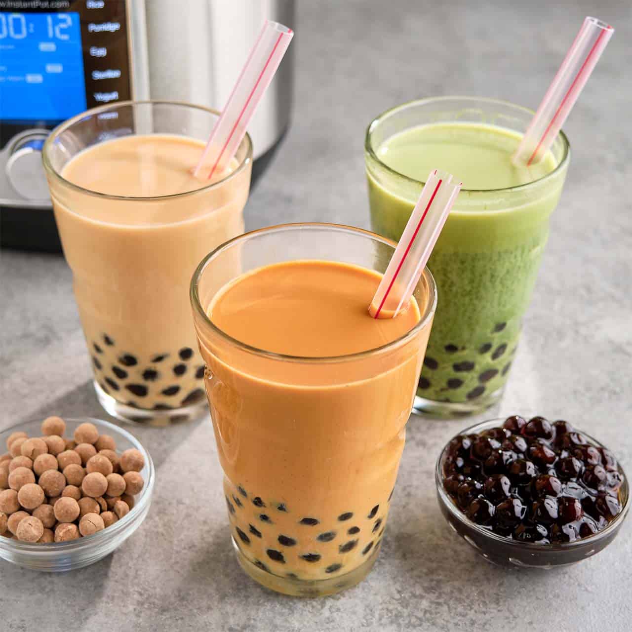 Three colorful glasses of boba tea, with cooked and uncooked boba pearls in dishes, and an Instant Pot in the background.
