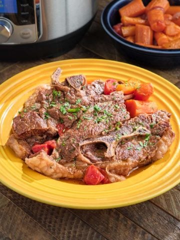 A plate of lamb shoulder chops, sprinkled with parsley, with carrots and tomatoes on the side