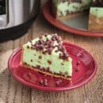 A plate with a slice of mint chocolate chip cheesecake, sprinkled with more chocolate chips, and an Instant Pot in the background