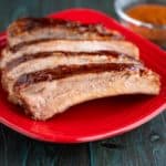 Individual spare ribs brushed with sauce on a red plate with a bowl of barbecue rub in the background