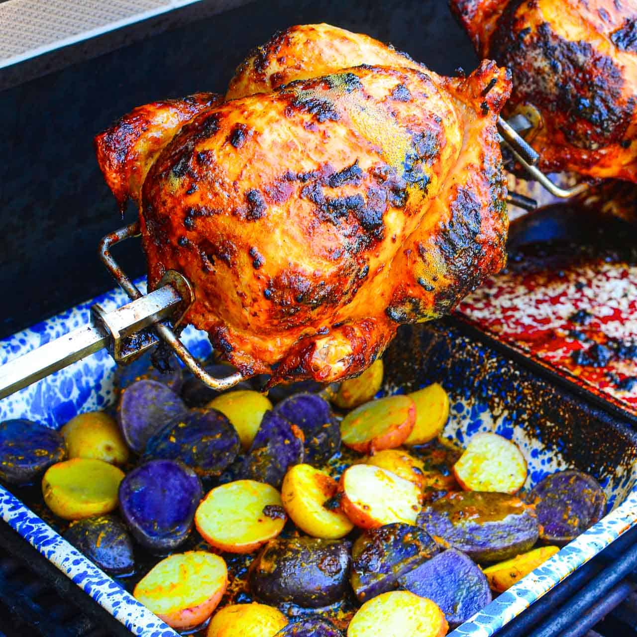 Pollo a la Brasa, Peruvian Rotisserie Chicken, grilling on a rotisserie, with a drip pan full of potatoes underneath