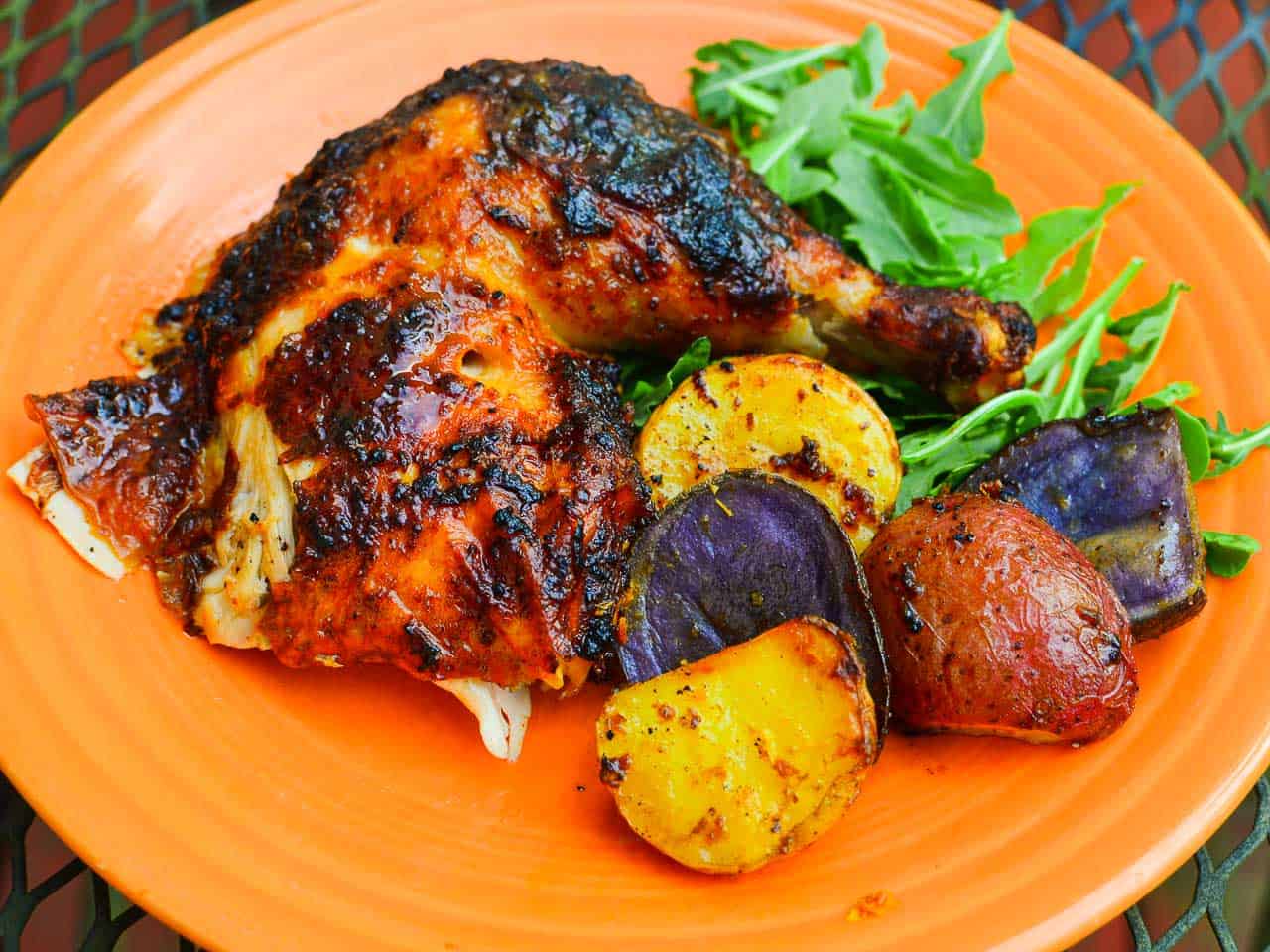 A plate with a cooked leg of Pollo a la Brasa, with purple, red, and yellow potatoes