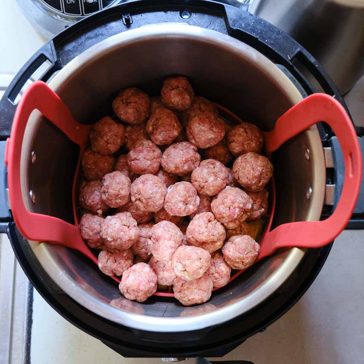 An Instant Pot with a red baking sling covered with uncooked meatballs