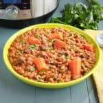 A bowl of lentil and beef stew with an Instant Pot and parsley in the background