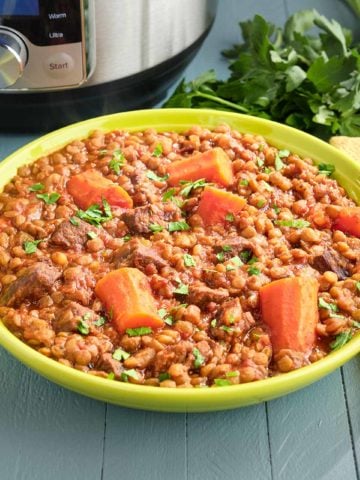 A bowl of lentil and beef stew with an Instant Pot and parsley in the background