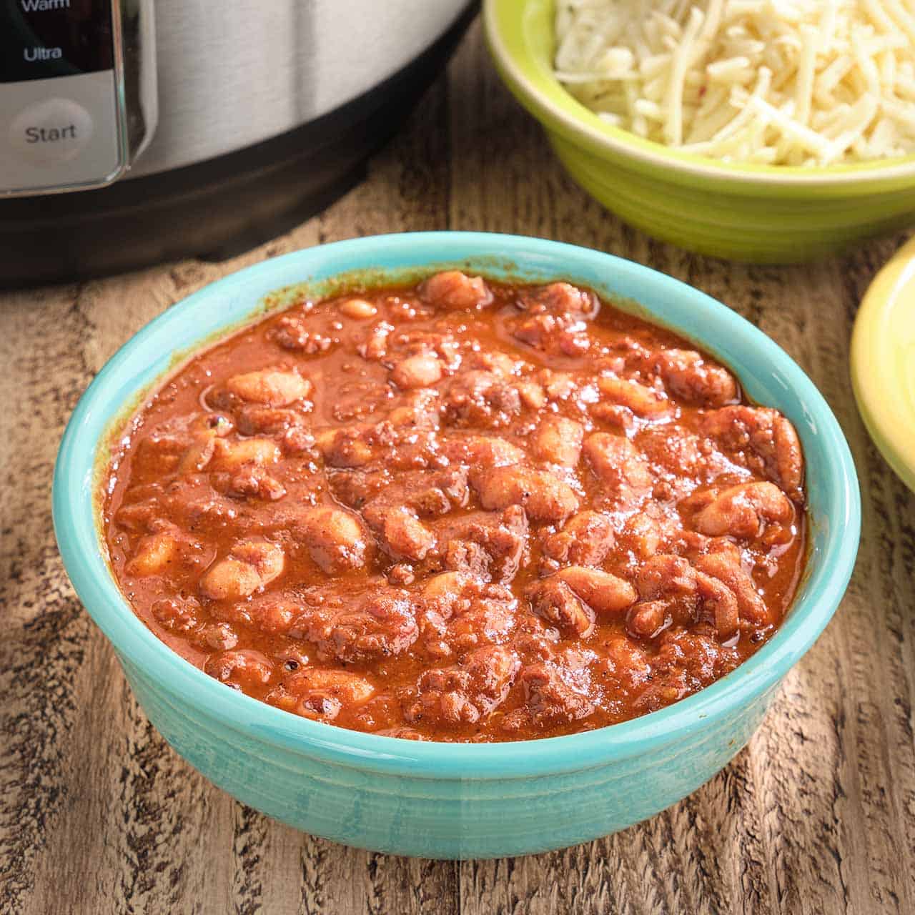 A bowl of chorizo chili with pinto beans, with an Instant Pot and bowl of shredded cheese in the background