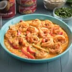 A bowl of thai red shrimp curry with cans of coconut milk and red curry paste in the background