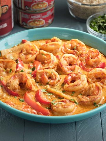 A bowl of thai red shrimp curry with cans of coconut milk and red curry paste in the background