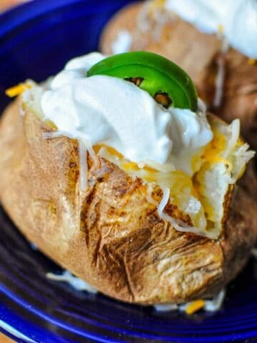 A baked potato loaded with cheese, sour cream, and a jalapeno slice