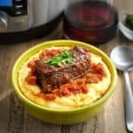 A boneless beef short rib covered in wine sauce on a bed of polenta