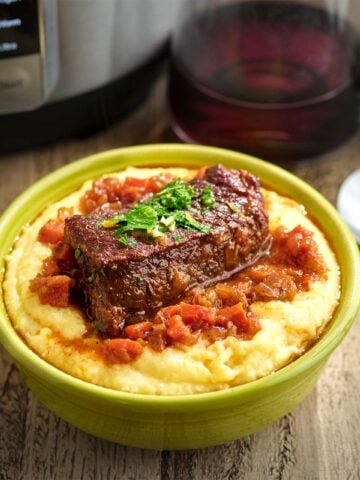 A boneless beef short rib covered in wine sauce on a bed of polenta