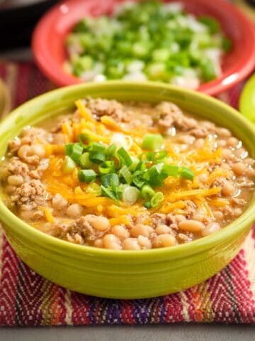 A bowl of white turkey chili with cheese and green onions sprinkled on top