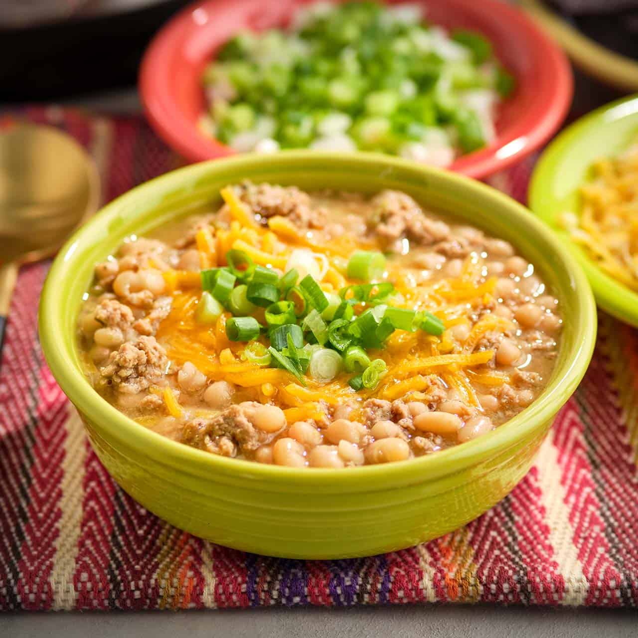 A bowl of white turkey chili with cheese and green onions sprinkled on top