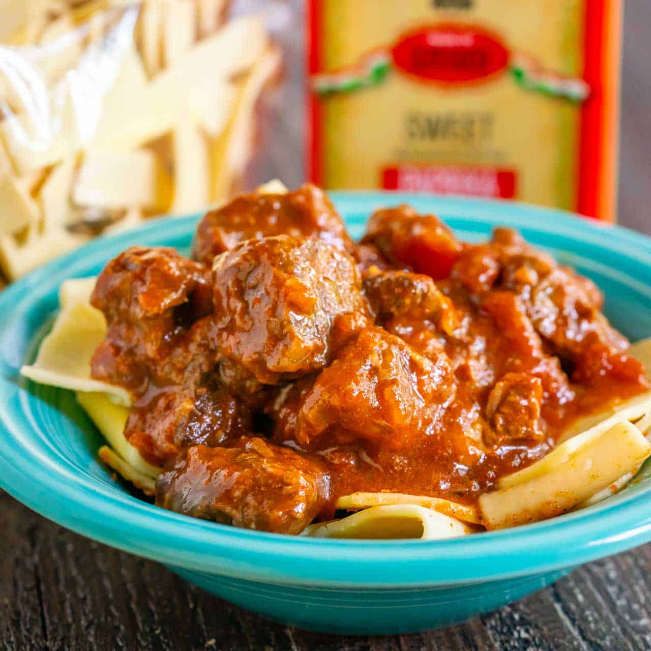 A bowl of beef goulash with egg noodles and paprika in the background